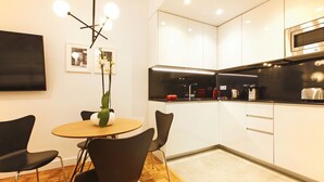 A modern kitchen with white cabinets, a black countertop, and a round wooden table with black chairs. - Malasaña Downtown (Madrid)
