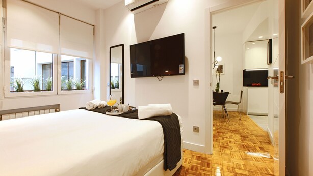 A hotel room with a large bed, a flat-screen TV mounted on the wall, a window with a view of the outside, and a wooden floor. - Malasaña Downtown (Madrid)