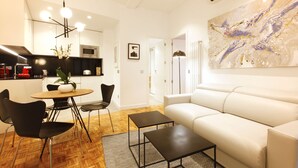 A modern living room with a white sofa, a dining area with a round table and chairs, and a kitchen with a microwave. - Malasaña Downtown (Madrid)