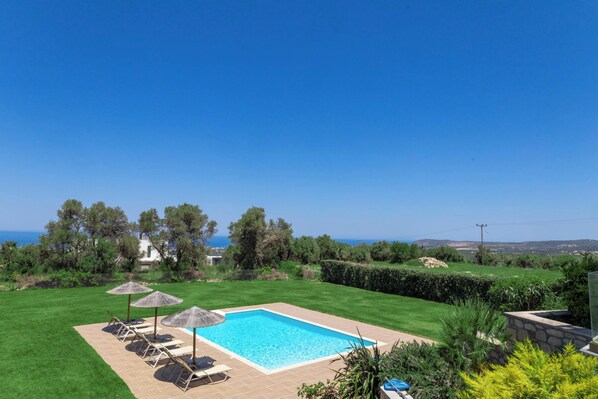 A rectangular swimming pool with a clear blue pool, surrounded by a well-maintained lawn, and a view of the sea in the background. - Villa Litinas - A 2,500sqm Escape Amid Olive Groves (Rethymno)