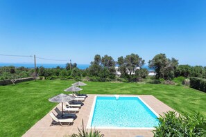 A rectangular swimming pool with a clear blue water surface, surrounded by a wooden deck. There are lounge chairs and umbrellas along the poolside. - Villa Litinas - A 2,500sqm Escape Amid Olive Groves (Rethymno)