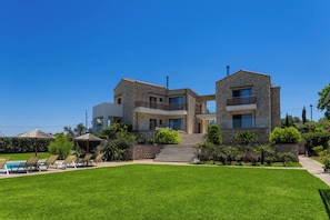 A two-story stone house with a swimming pool, outdoor seating, and a well-maintained lawn.
