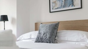 A neatly made bed with white linens and a grey marble-patterned pillow, a black lamp on a bedside table, and a framed abstract painting on the wall. - Magnolia House - Townhouse in Old Town Poole (Poole)
