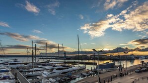 Una marina con diversi yacht ormeggiati, un bacino d'acqua calma e un cielo sereno con nuvole.