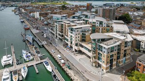 Una marina con imbarcazioni ormeggiate, una passeggiata sul lungomare e edifici moderni con spazi commerciali.