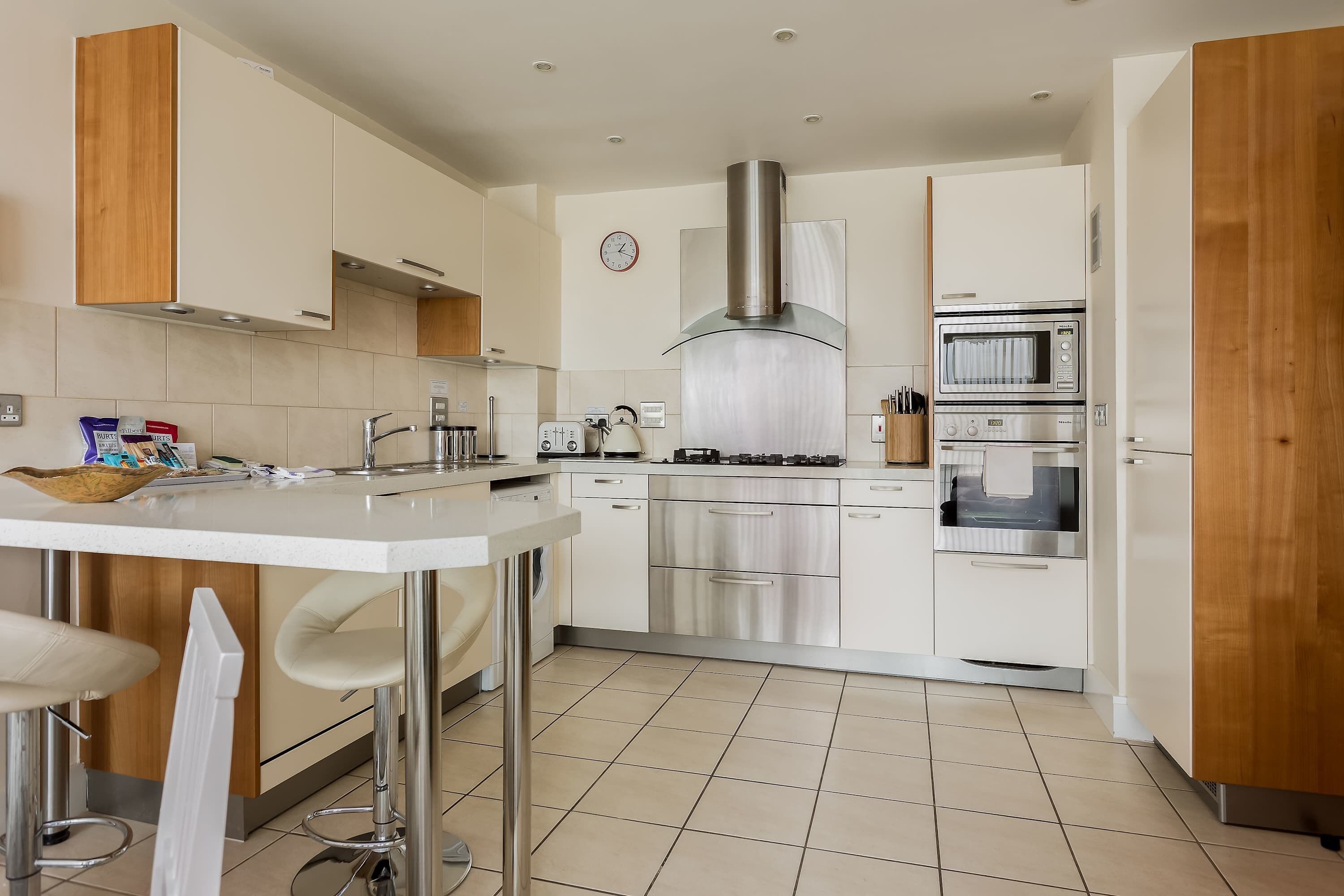 A modern kitchen with white cabinets, stainless steel appliances, and a bar area.