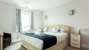 Una camera da letto ordinata con un letto, comodini, una sedia e una finestra con tende.
