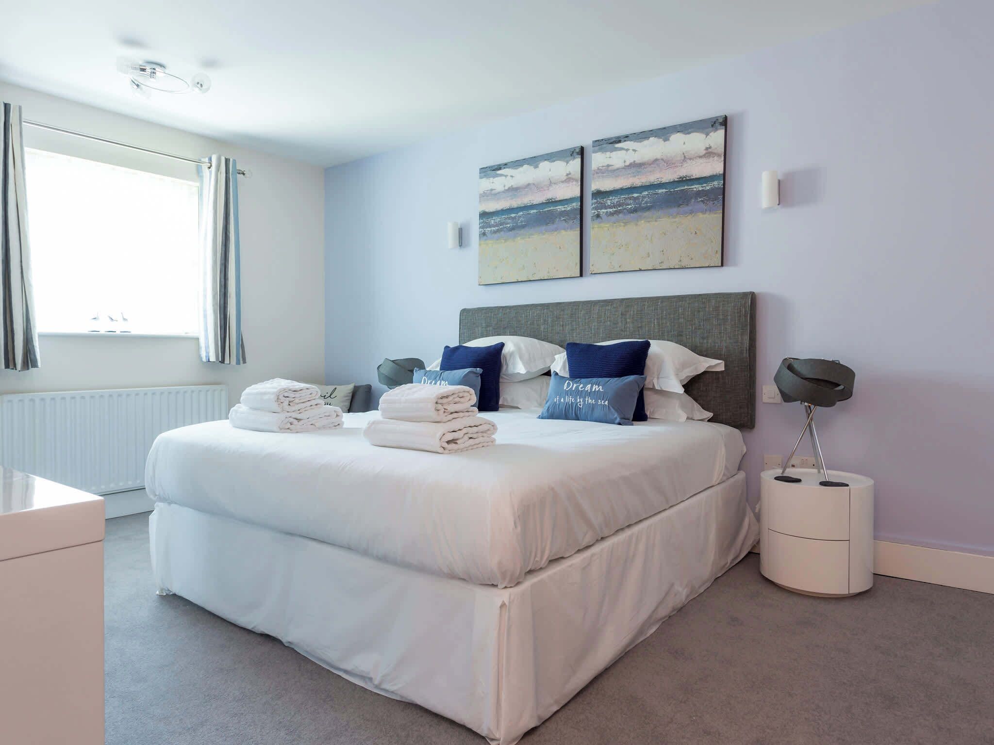 A neatly made bed with pillows, a bedside lamp, and a view of the beach through the window.
