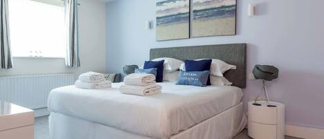 A neatly made bed with pillows, a bedside lamp, and a view of the beach through the window.