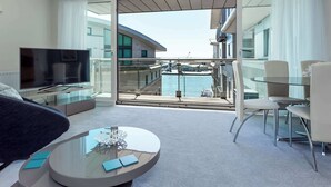 A modern hotel room with a balcony, a TV, a glass coffee table, and a seating area. - Jibe Ho - Spacious Apartment with Harbour Views (Poole)