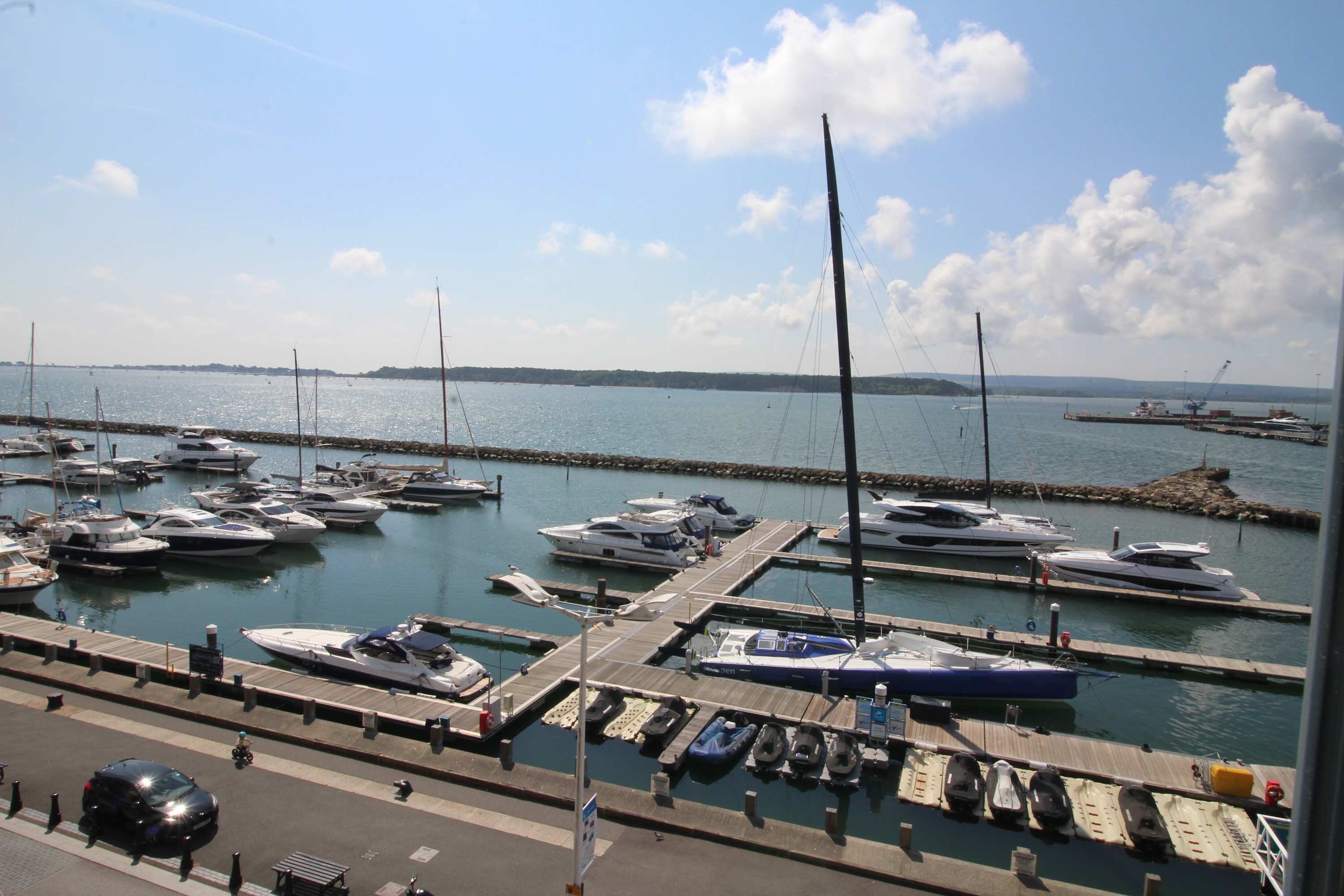 A marina with boats docked at wooden piers, a clear sky, and a distant shoreline.
