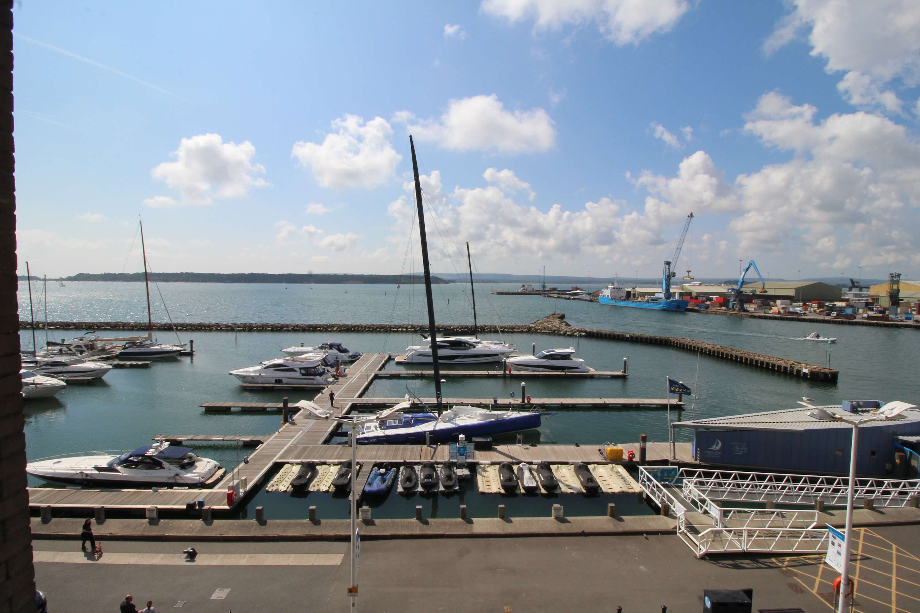 A marina with boats docked, a pier, and a building with a crane.
