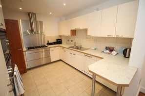 Una cocina moderna con electrodomésticos de acero inoxidable, armarios blancos y piso de baldosas.