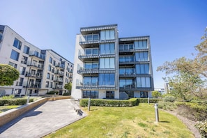 A modern multi-story residential building with balconies, a paved walkway, and a well-maintained lawn.