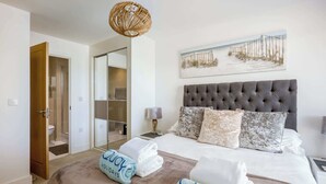 A hotel room with a large bed, a grey tufted headboard, and a beach-themed painting on the wall. - Sea Breeze - Close to Bournemouth Beach (Bournemouth)