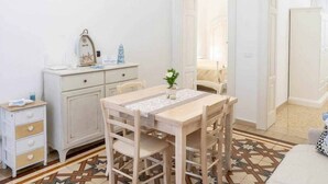 A room with a wooden dining table, white cabinets, a small bedside table, and a patterned rug. - WePuglia - Domus Neptuni (Monopoli)