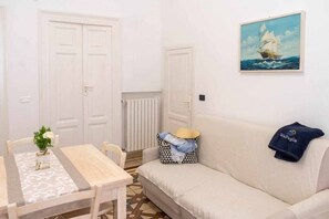 A room with a dining table, a sofa, a painting of a sailboat, and a radiator. - WePuglia - Domus Neptuni (Monopoli)