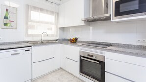Une cuisine moderne avec des meubles blancs, un four encastré, un four à micro-ondes et une fenêtre avec un rideau.