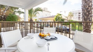 Une table ronde blanche, recouverte d’aliments pour le petit-déjeuner, des chaises blanches et une rambarde de balcon.
