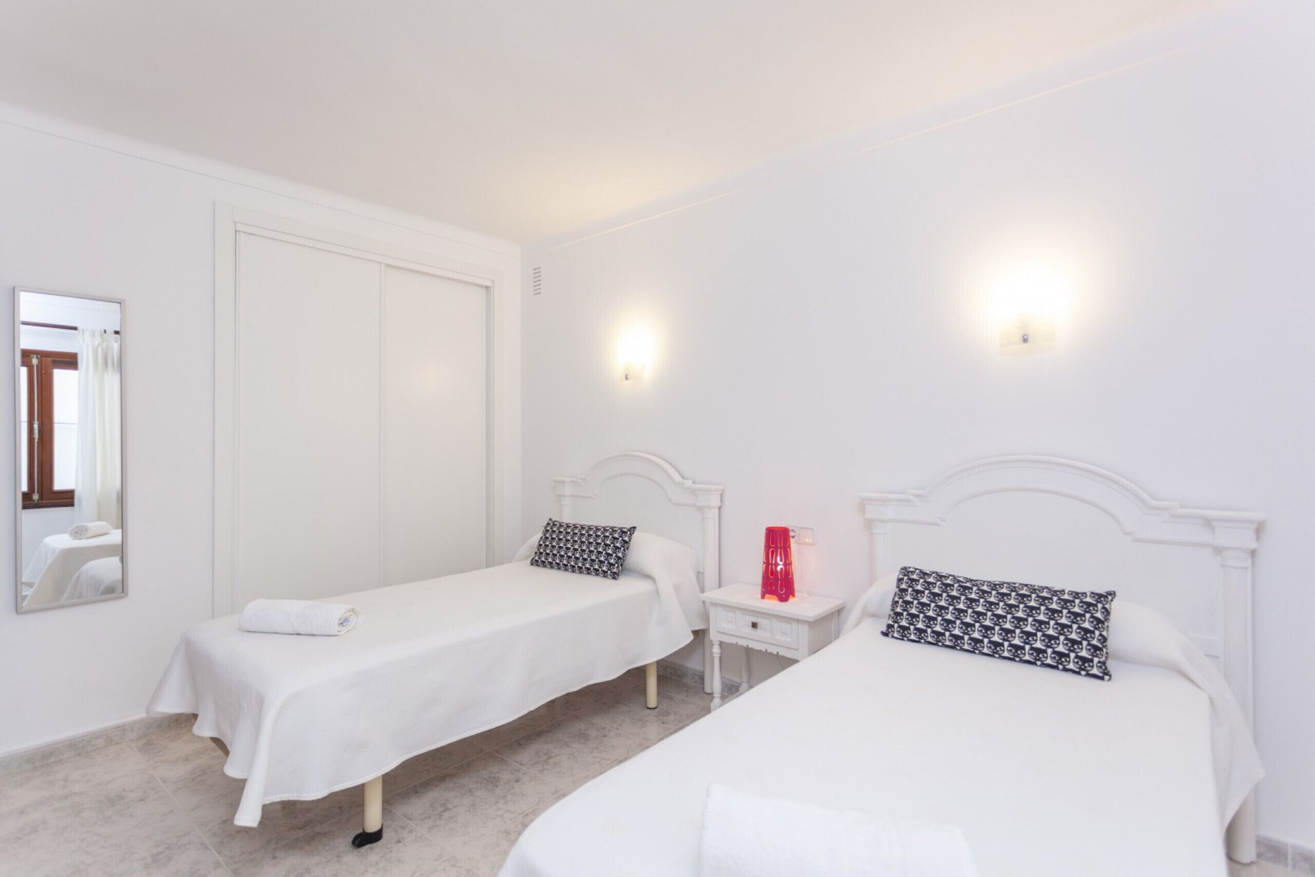 Une chambre d’hôtel avec deux lits simples, une table de chevet avec une lampe, un miroir et une armoire.