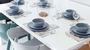 A dining table set with blue plates, bowls, and cutlery, accompanied by wine glasses and coasters.