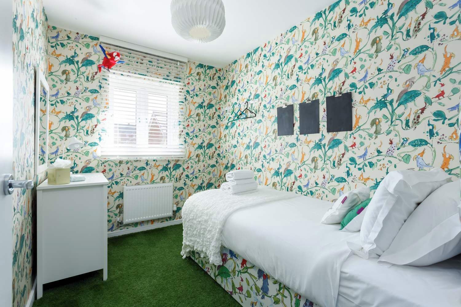 A bedroom with floral wallpaper, a bed with white bedding, a small bedside table, and a radiator.