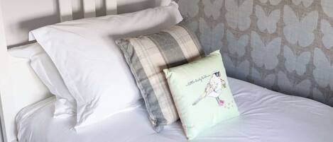 Un lit avec une literie blanche, un coussin à carreaux et un coussin orné d’une illustration d’oiseau.