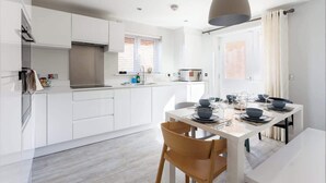 A modern kitchen with white cabinets, a built-in oven, and a dining area with a table set for four.