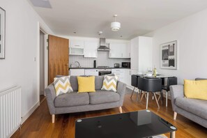 Ein modernes Wohnzimmer mit einem grauen Sofa, einem schwarzen Couchtisch und einem Essbereich mit schwarzem Tisch und Stühlen.
