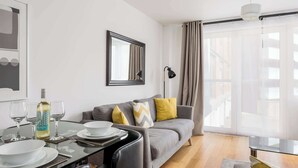 A modern living room with a dining area, a sofa with cushions, a glass table, and a large window with curtains. - Castle Lanes - Minutes from Poole Quay (Poole)