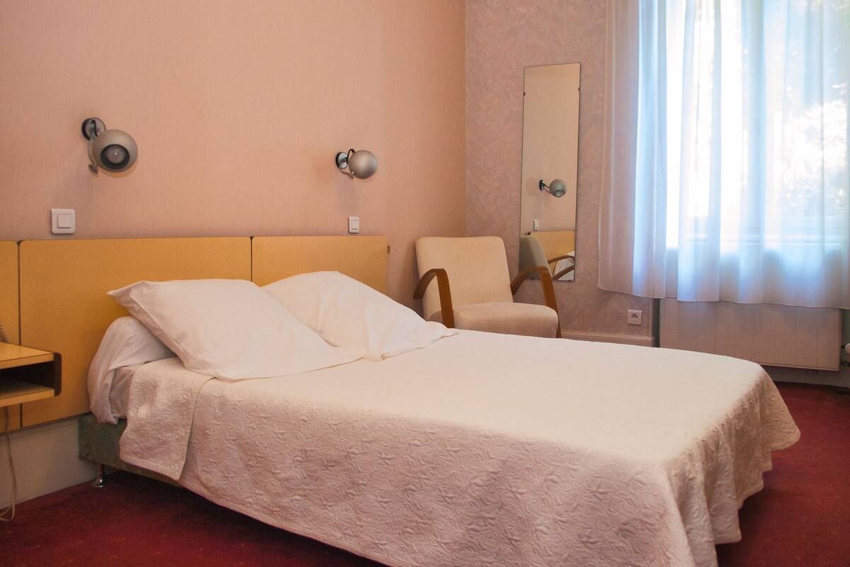 A hotel room with a bed, a chair, a nightstand, and a mirror.