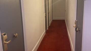 A narrow hallway with red carpet, white walls, and doors with brass handles.