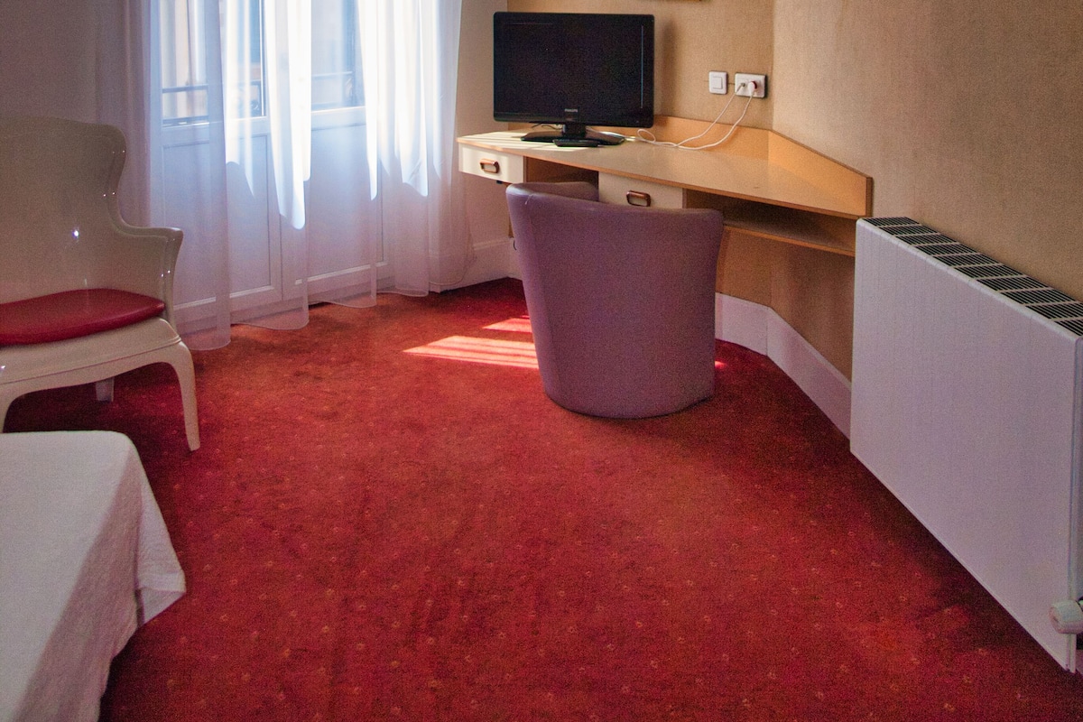 A room with a desk, chair, and a large window with curtains.