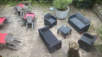 Un patio exterior con mobiliario de mimbre, una planta en maceta y una mesa de piedra.