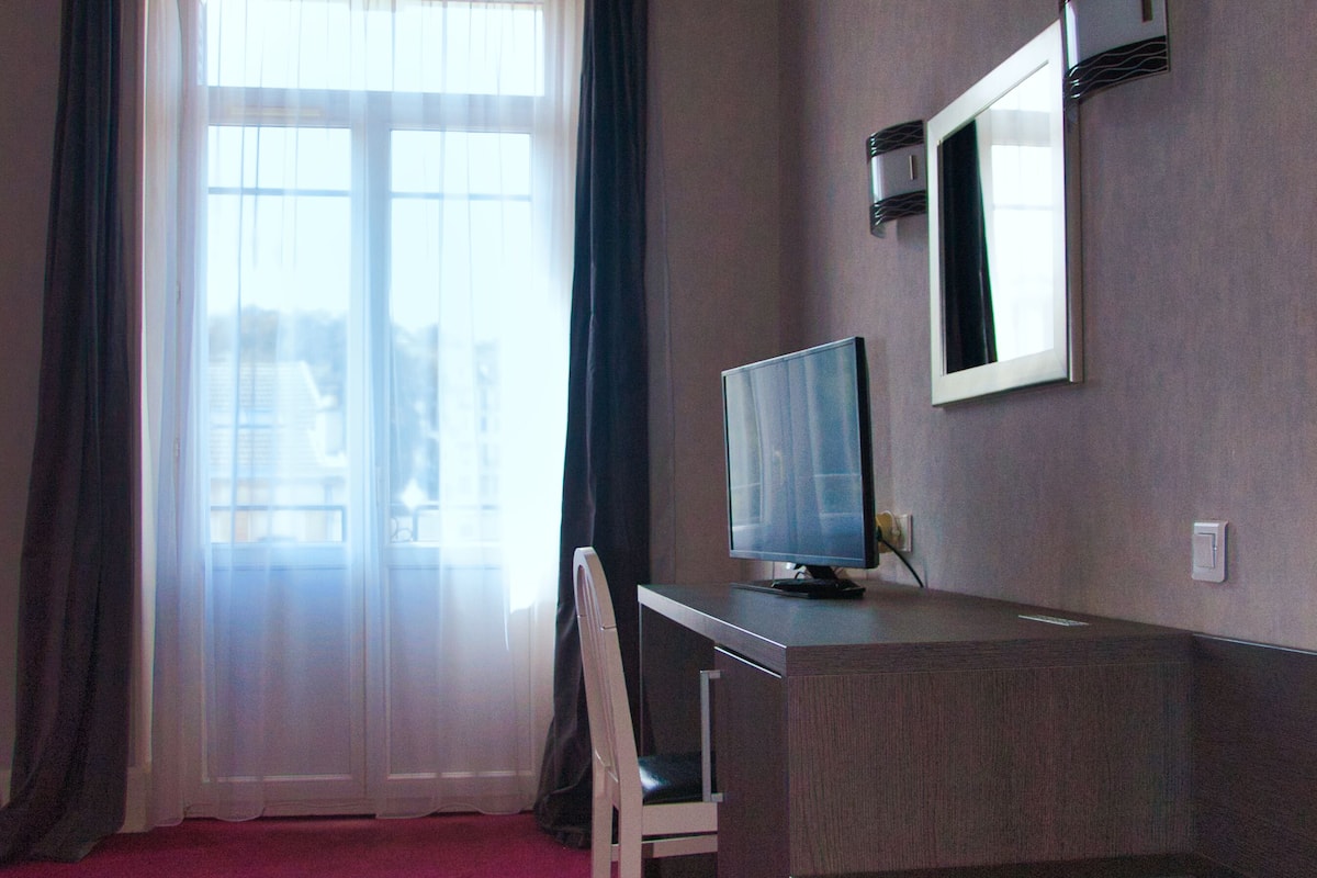 A hotel room with a desk, chair, and a large window with curtains.