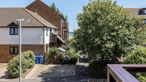 A residential building with a brick facade, a tiled roof, and a balcony. There are blue bins near the entrance and a tree in the foreground. - Sanderling - Close to Poole Quay and Baiter Park (Poole)