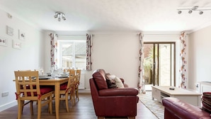 A dining area with a wooden table and chairs, a red leather sofa, and a small kitchen area. - Sanderling - Close to Poole Quay and Baiter Park (Poole)