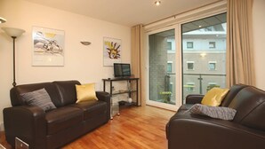 A modern living room with two dark brown sofas, a glass door leading to a balcony, and artwork on the walls. - Marina Secret - with Free Parking (Poole)
