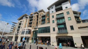 A multi-story building with balconies, a café named "Quay Café," and a pedestrian area with people walking and a cyclist. - Marina Secret - with Free Parking (Poole)