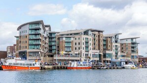 A modern multi-story building with balconies, located near a waterfront with boats docked. - Marina Secret - with Free Parking (Poole)