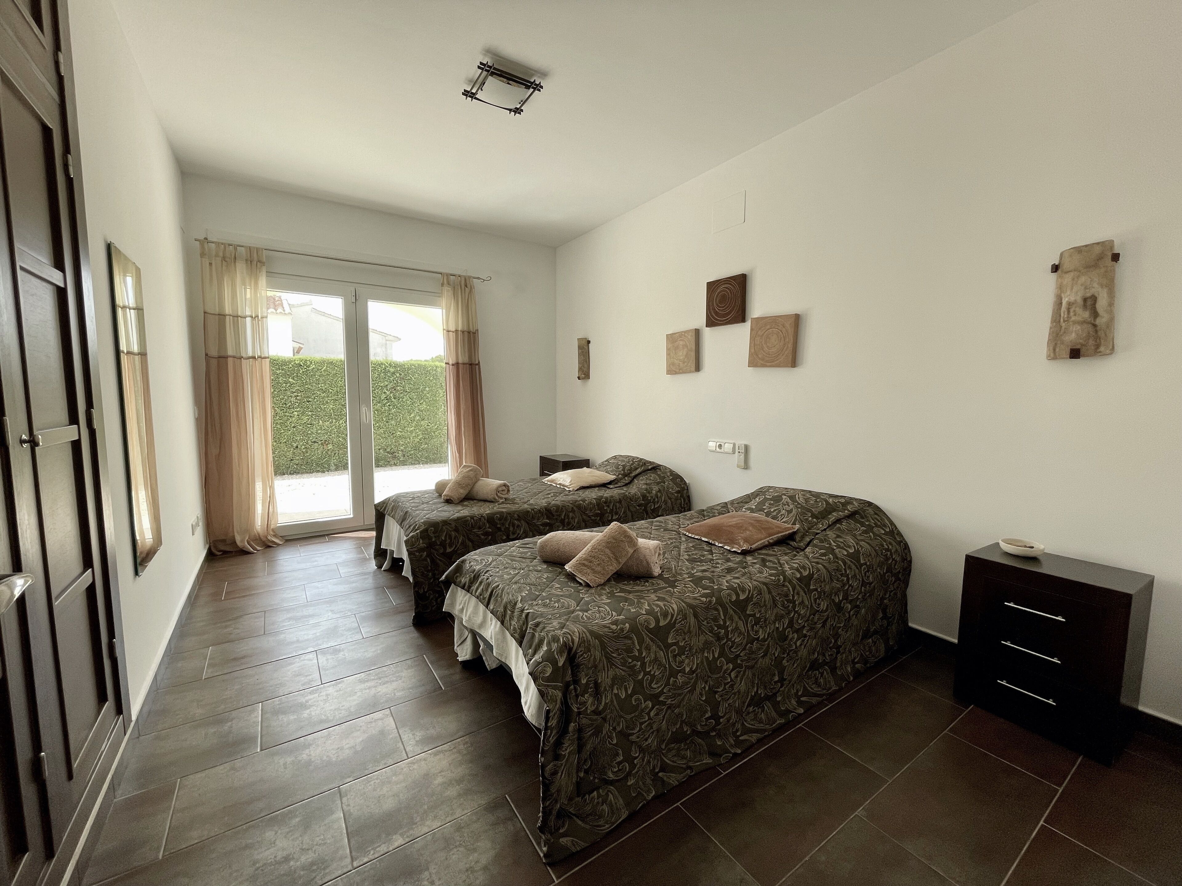 Um quarto com duas camas, uma porta de correr de vidro que dá para uma varanda e uma pequena mesa de cabeceira com abajur.