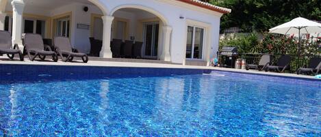 A swimming pool with lounge chairs and a covered patio area.