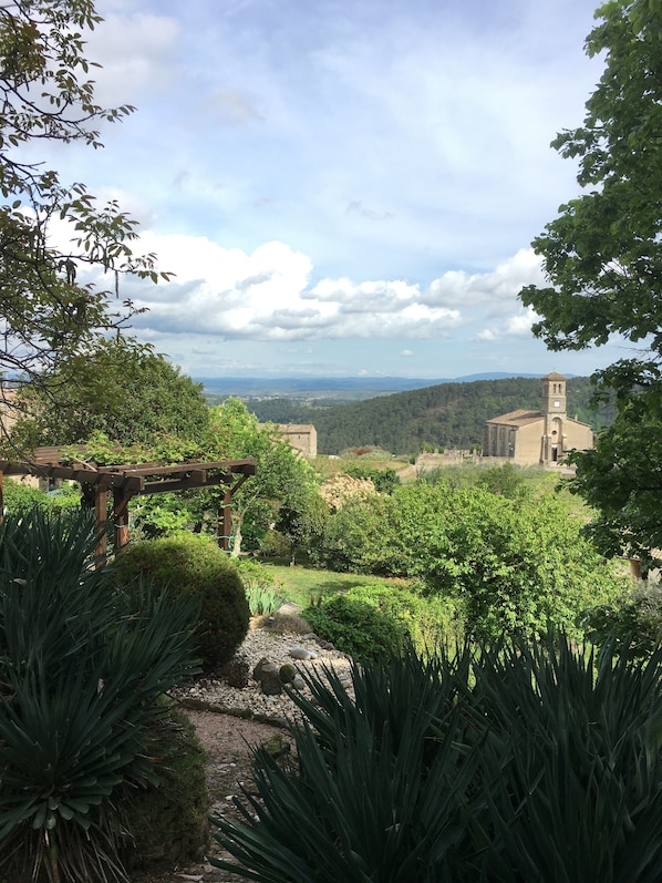 A garden with a pergola, various plants, and a view of distant buildings.