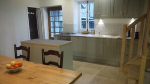 Una cocina con una mesa de madera, sillas, un cuenco de fruta y una ventana.