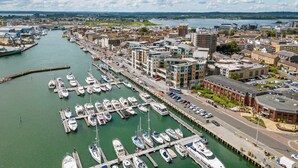 A marina with numerous boats docked, connected to a cityscape with modern buildings and a river. - Riva -180-Degree Panoramic Views from Balcony (Poole)