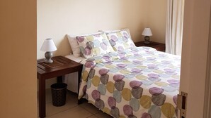 Ein Schlafzimmer mit einem Bett, zwei Nachttischen mit Lampen, einem Mülleimer und einer Deckenleuchte.
