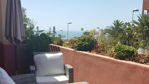Eine Terrasse mit Korbmöbeln, Blick aufs Meer und ein Gebäude im Hintergrund.