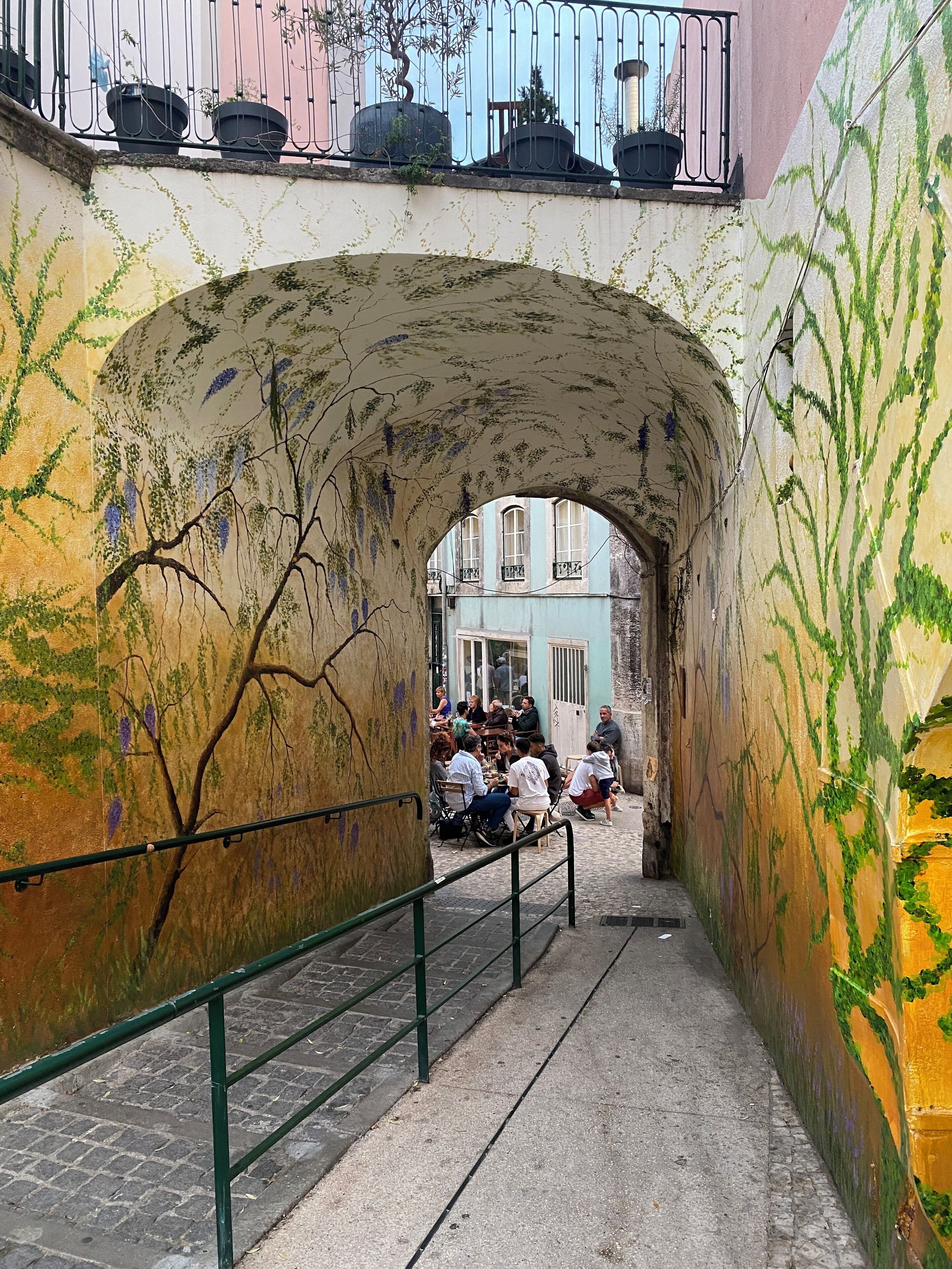 Ein Café mit Außenbereich, einem Steinkorbbogen, Sitzgelegenheiten und Blick auf die Straße.