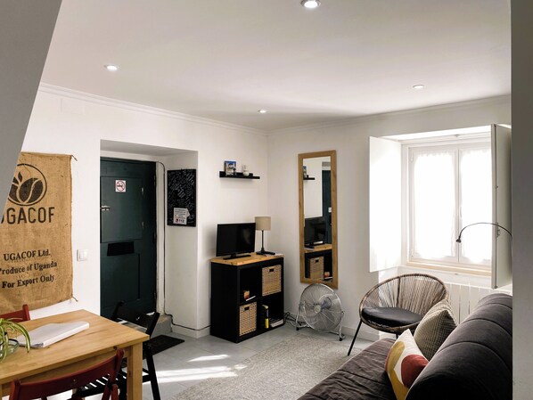 A compact living space with a dining area, a television, a fan, and a window with curtains.