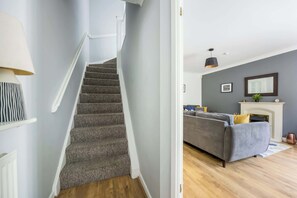 A staircase with carpeted steps leading to a room with a grey sofa, a fireplace, and a hanging light fixture. - Palma - Coastal Home near Harbour and beach (Poole)